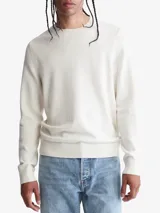 Sweater de punto liso color blanco hueso, con cuello redondo y puños y dobladillo en punto canalé. Presenta un pequeño logo bordado en el pecho.