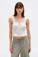 Musculosa de viscosa color negro con estampado de lunares blancos, tirantes anchos con volados fruncidos, escote cuadrado con cordones ajustables en el centro y cuerpo elástico con punto smock.