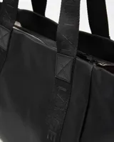 Cartera tipo tote de color negro con asas de hombro decoradas con inscripciones grabadas y detalle de aplique circular con logo en la parte frontal.