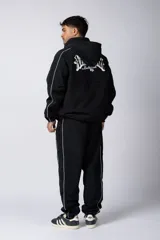 Campera deportiva negra con cierre frontal, capucha ajustable y detalles de líneas blancas en las mangas. Presenta el logo de la marca bordado en el pecho.