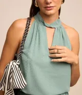 Blusa sin mangas color verde menta, confeccionada en tejido jacquard con textura de pequeños cuadros. Presenta un cuello halter que se anuda o cruza en la parte delantera, creando un escote en V con un recorte central.