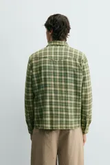 Camisa de corte relajado confeccionada en tejido de algodón con estampado de cuadros en tonos verdes y beige. Presenta cuello solapa, cierre frontal con botones a presión, bolsillos plastrón en el pecho y mangas largas con puños abotonados.