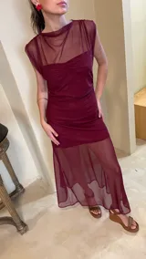 Vestido largo de microtul bordó, sin mangas, con escote alto tipo buche y diseño transparente con forro corto interno que genera un efecto translúcido en la falda.