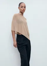 Poncho de tejido ligero y traslúcido en color beige, con diseño asimétrico y corte holgado.