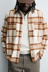 Camisa de corte relajado confeccionada en tejido con acabado de franela. Presenta diseño de cuadros en tonos beige, marrón y amarillo, cuello solapa, manga larga con puños abotonados, bolsillos plastrón en el pecho y cierre frontal de botones.