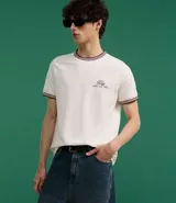 Remera blanca de algodón, corte baby tee, con cuello redondo y mangas cortas con ribete doble en bordó. Estampa pequeña con texto "The Staff" en el pecho.