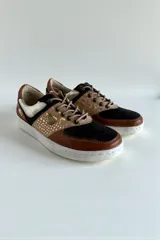 Championes de diseño urbano con combinación de tonos marrones, negros y detalles metalizados, puntera de cuero y suela blanca.