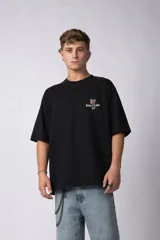 Remera de corte oversize color negro, confeccionada en algodón premium de alto gramaje. Presenta un diseño minimalista con un pequeño estampado frontal que incluye un oso y el texto Richer & Louder VCP.