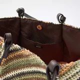 Bolso tipo capazo grande de tejido trenzado con diseño de rayas diagonales multicolor en tonos verdes, marrones, blancos y negros. Cuenta con doble asa de hombro en cuero sintético marrón.