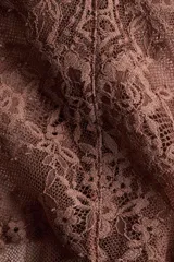 Body de encaje color marrón, con escote en V pronunciado y breteles anchos con detalle de encaje festoneado. Presenta copas sin forro ni aros y un refuerzo interior con botones a presión ocultos en la parte inferior.