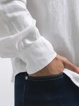 Camisa de manga larga, color blanco, con cuello camisero y botones frontales. El tejido presenta una textura visible de lino.