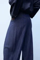 Pantalón confeccionado con lino de tiro alto con pliegues delanteros y cinco bolsillos. Presenta pernera holgada y cierre frontal con cremallera, botón interior y gancho.