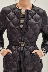 Campera acolchada de diseño matelassé con cierre frontal y cinturón ajustable con hebilla metálica. Presenta cuello redondo y mangas largas con puños elásticos.