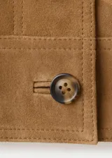 Chaqueta de ante color marrón claro, de diseño corto y recto, con cuello camisero, manga larga, dos bolsillos de parche delanteros y cierre frontal con botones.