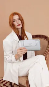 Billetera larga de diseño rectangular con solapa frontal y cierre magnético. Presenta un acabado metalizado plateado y el logo de la marca grabado en la parte frontal. Incluye compartimentos internos para tarjetas y monedero con cierre.