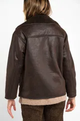 Campera tipo gamulan de corte oversize, color marrón oscuro con interior y solapas de corderito al tono. Presenta cierre frontal y mangas largas.