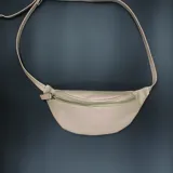 Riñonera color beige, con correa larga regulable y cierre superior con cremallera.