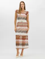 Vestido midi confeccionado en tejido de punto calado, con patrón geométrico en zigzag en tonos blanco, marrón, tostado y azul. Presenta escote a la base, mangas cortas con volados en los hombros, silueta recta y forro interior a tono. Incluye un cinturón fino con hebilla metálica.