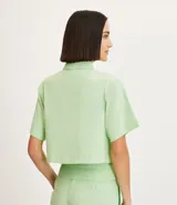Camisa color verde claro de crepé, con cuello camisero, abotonado delantero, mangas cortas y solapas delanteras aplicadas.