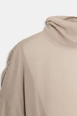 Body de cuello subido con mangas largas abullonadas y puños elásticos. Presenta un diseño combinado con paneles de tela semitransparente en la parte superior y cierre inferior con botones a presión.