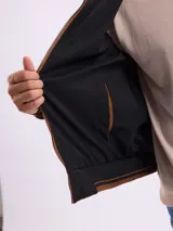Campera reversible de gamuza sintética color marrón, con cierre frontal, cuello alto y puños de tejido acanalado con detalles de rayas.