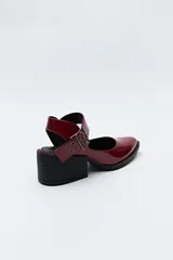 Zapato negro tipo zueco con acabado charol, tira ancha con hebilla metálica y taco ancho de altura media.