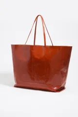 Bolso shopper de estructura blanda confeccionado en piel vacuna con acabado brillante. Cuenta con doble asa de hombro, costura central vertical y logo metálico de la marca en la base frontal.