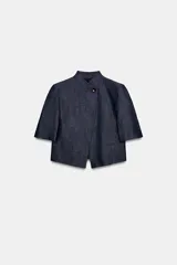 Blazer de manga corta confeccionado en lino, color azul marino, con cuello alto, cierre cruzado con un botón y pespuntes en contraste de color rojo. Cuenta con hombreras y bolsillos delanteros ribeteados.