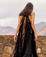 Vestido largo negro de viscosa fluida con cuello halter y espalda descubierta. Presenta un diseño vaporoso con un panel frontal y trasero con estampado difuminado en tonos tostados y azulados, y un volante fruncido en el bajo.