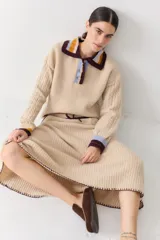 Falda midi de lana en color marrón, con diseño acampanado y tejido acanalado. Presenta una cintura elástica con cordón de ajuste, detalles de rayas en tonos beige y blanco en la parte superior, y costuras decorativas en el ruedo.