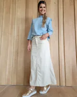 Pollera larga de corte recto en denim color arena, con diseño de cinco bolsillos, cierre frontal con botón y costuras a la vista.