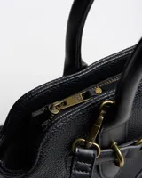 Cartera tipo tote bag color negro de símil cuero con textura granulada, asas de mano y correa bandolera ajustable. Cuenta con herrajes dorados envejecidos y tira decorativa frontal con hebilla.