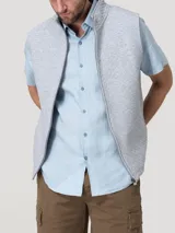 Chaleco gris melange con textura acolchada de rombos, cuello alto y cierre frontal de cremallera. Presenta un pequeño parche bordado con silueta de pato en el pecho.