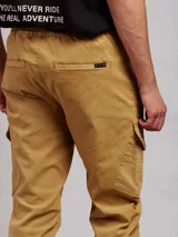 Pantalon cargo de sarga color tostado, con cintura elástica y cordón de ajuste, bolsillos laterales con solapa y puños elásticos en los tobillos.