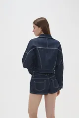 Campera de jean de corte cropped, color azul oscuro con costuras en contraste. Presenta cuello clásico, cierre frontal con botones metálicos y bolsillos frontales con solapa.