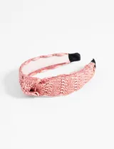 Vincha rígida color salmón con textura tejida de rafia y nudo en la parte superior.