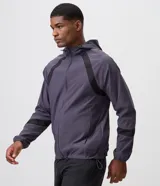 Campera deportiva Get Over de poliéster tecnológico, de color gris oscuro con bandas negras decorativas en los hombros y mangas. Cuenta con capucha ajustable, cierre frontal con cremallera, y puños y cintura elastizados.