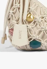 Cartera baguette de cuero color beige con diseño trenzado tipo red y apliques de cuentas de colores y formas metálicas en el cuerpo y en la manija. Cuenta con cierre superior y etiqueta colgante de la marca.