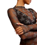 Top de manga larga confeccionado en malla transparente con diseño bicolor y bordado floral. Presenta cuello tipo mock, detalle de orificios para los pulgares y ruedo con vuelo, de silueta relajada y sin forro.