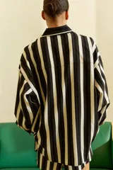 Camisa de manga larga con cuello y botones frontales, hombros caídos y canesú en la espalda. Presenta un patrón de rayas verticales en tonos negro, gris y blanco, con ribete blanco en el cuello.