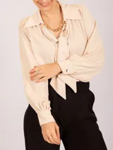 Blusa negra de manga larga con cuello camisero y lazo frontal. Presenta frunces en los hombros y puños ajustados con elástico.