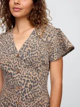 Vestido corto de denim con estampado de leopardo, corte entallado y falda acampanada. Tiene cuello en V, mangas cortas con volados y cierre frontal con botones.