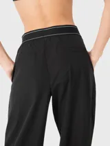 Pantalón de vestir negro de corte holgado y tiro medio, con cintura elástica estilo bóxer que presenta detalle de líneas blancas y logo bordado. Cuenta con pinzas delanteras y bolsillos laterales.
