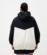 Campera cortavientos deportiva de Ashua, con diseño bicolor en negro y blanco. Presenta capucha integrada ajustable, cierre frontal con cremallera, mangas largas con puños elásticos y cintura elástica. Confeccionada en poliamida con forro de poliéster.