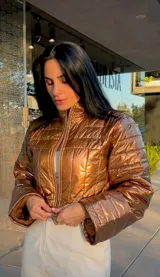 Chaqueta puffer corta de acabado metalizado en color ocre, con cuello alto, cierre frontal y mangas largas con puños amplios.