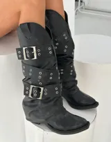 Botas de caña media color negro con efecto desgastado, diseño tipo western con múltiples correas ajustables con hebillas metálicas y detalles de ojales plateados.