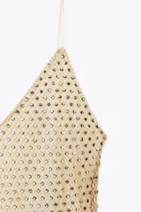 Vestido largo color dorado, confeccionado en tejido tipo red con aplicación de strass, escote pico y tirantes finos. Incluye forro interior y cierre en espalda con cremallera oculta en costura.