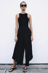 Mono largo negro con cuerpo de tejido ajustado sin mangas y cuello redondo, combinado con pantalón ancho de tejido fluido y satinado con diseño abullonado y bajo asimétrico. Cierre trasero con cremallera oculta.