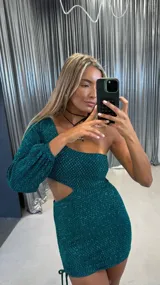 Vestido corto verde brillante con un hombro descubierto y una manga larga abullonada. Presenta un corte en la cintura y fruncido ajustable con cordón en un lateral de la falda.