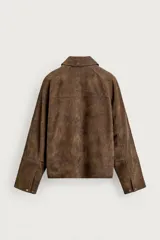 Cazadora de piel con acabado en ante color marrón, de corte relaxed fit, con cuello solapa, mangas largas con puños abotonados, bolsillos de vivo en pecho y cadera, y cierre frontal con cremallera oculta por solapa con botones a presión.